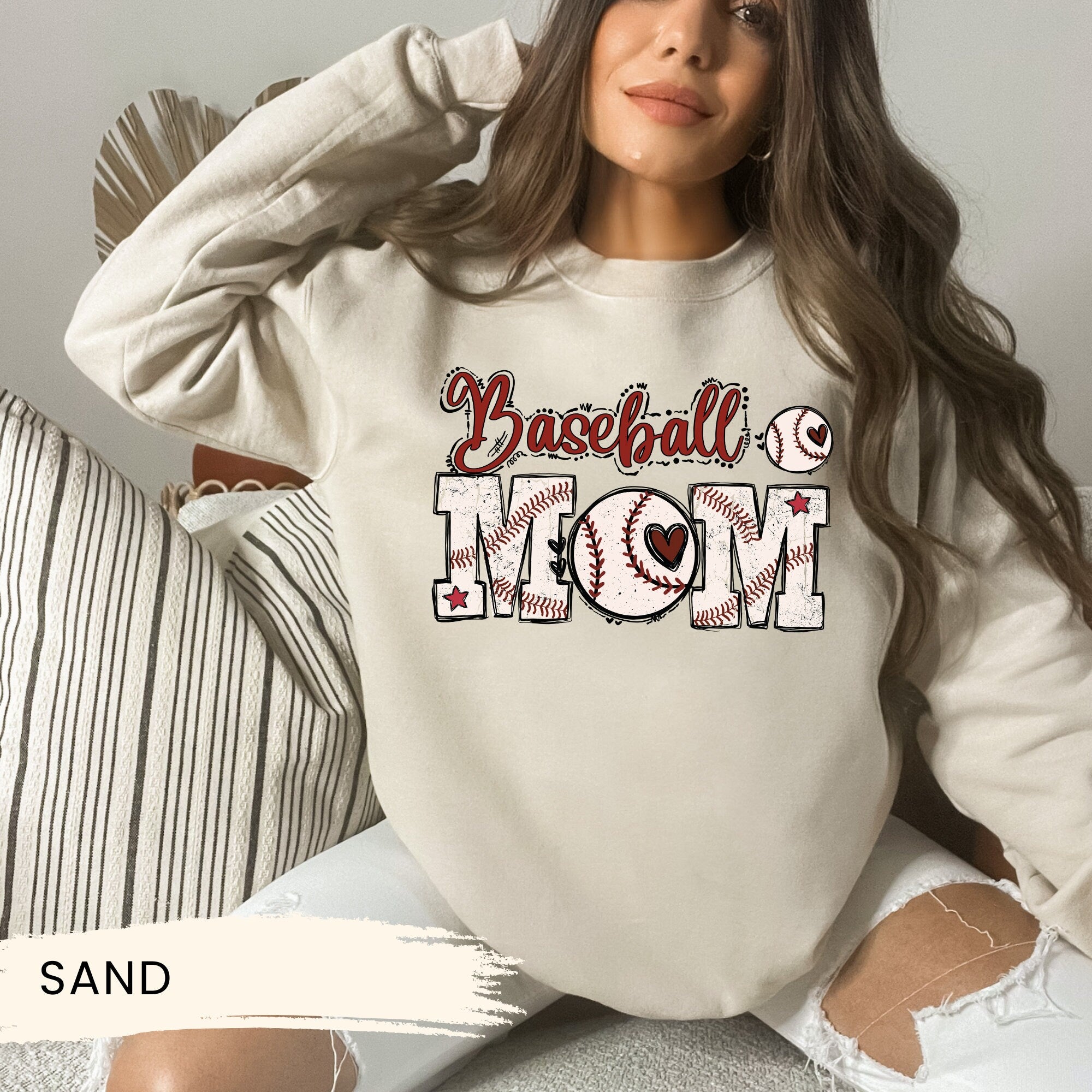 a woman sitting on a couch wearing a baseball mom sweatshirt