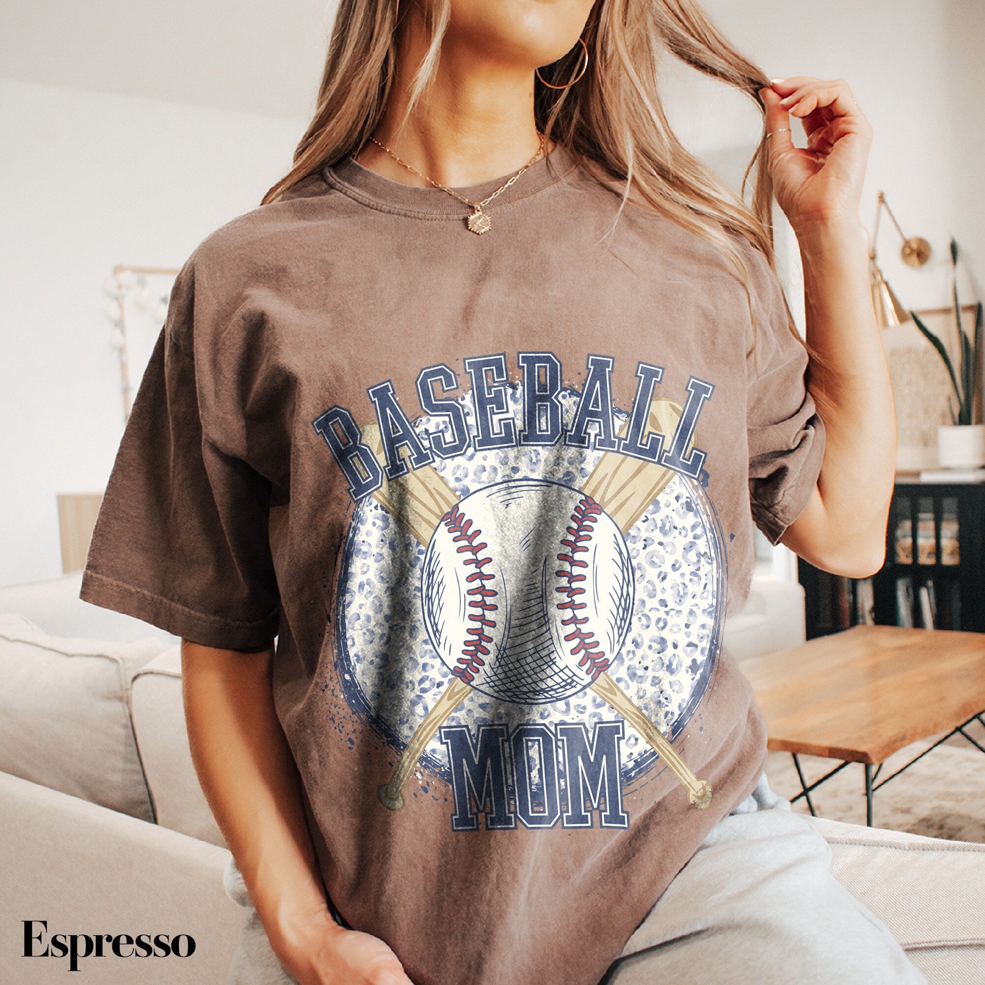 a woman sitting on a couch wearing a baseball mom shirt