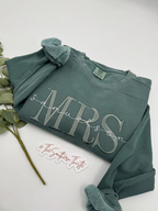 A green long-sleeved shirt with the text "Samuelson" printed on it, along with a small white sticker that says "@TheSouthernThistle".