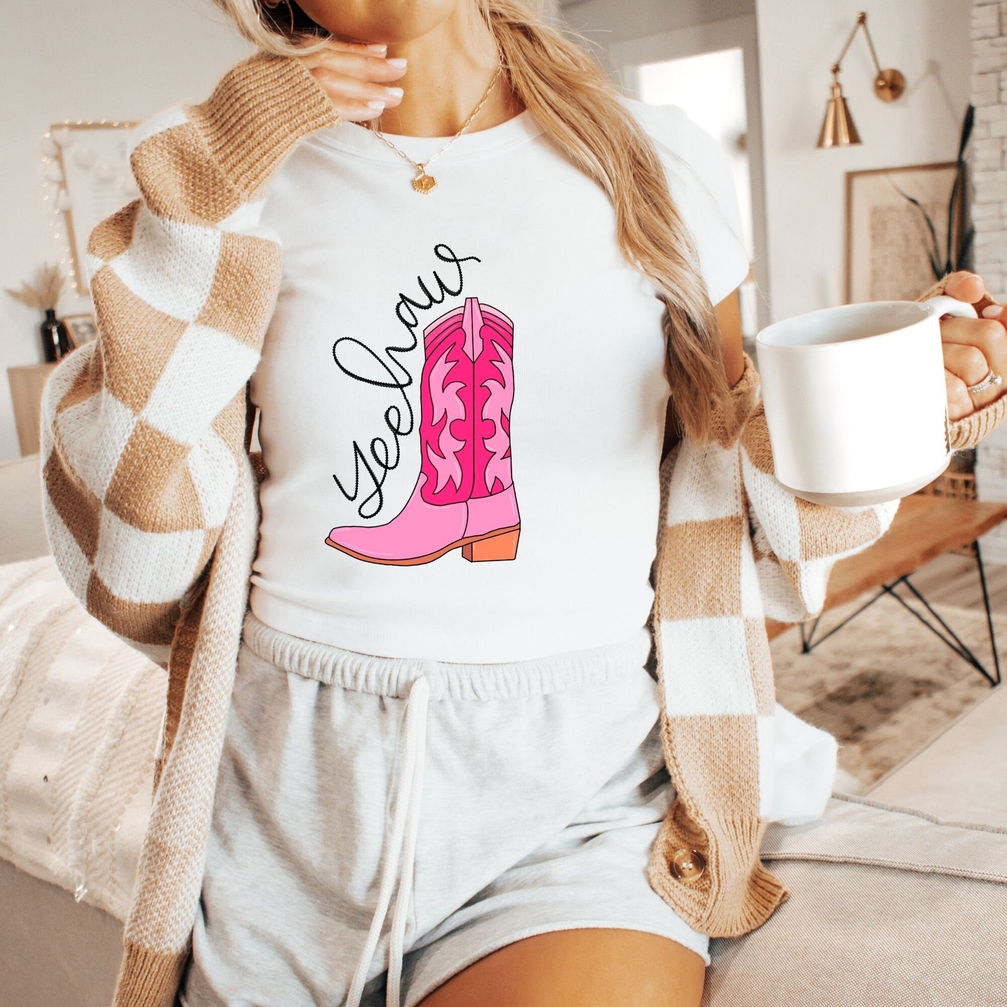 a woman holding a cup of coffee and wearing a pink cowboy boot t - shirt