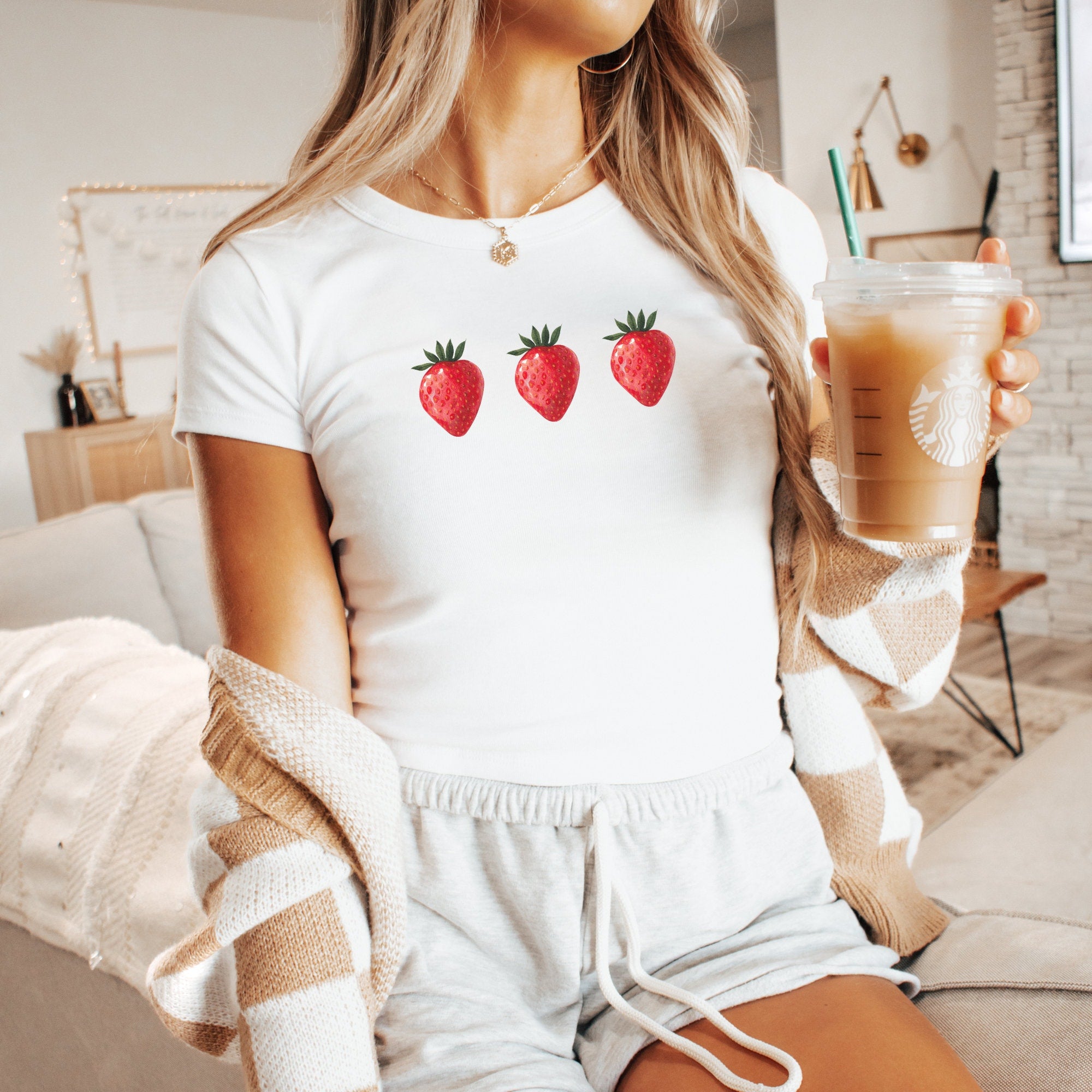 a woman holding a cup of coffee and strawberries on her shirt