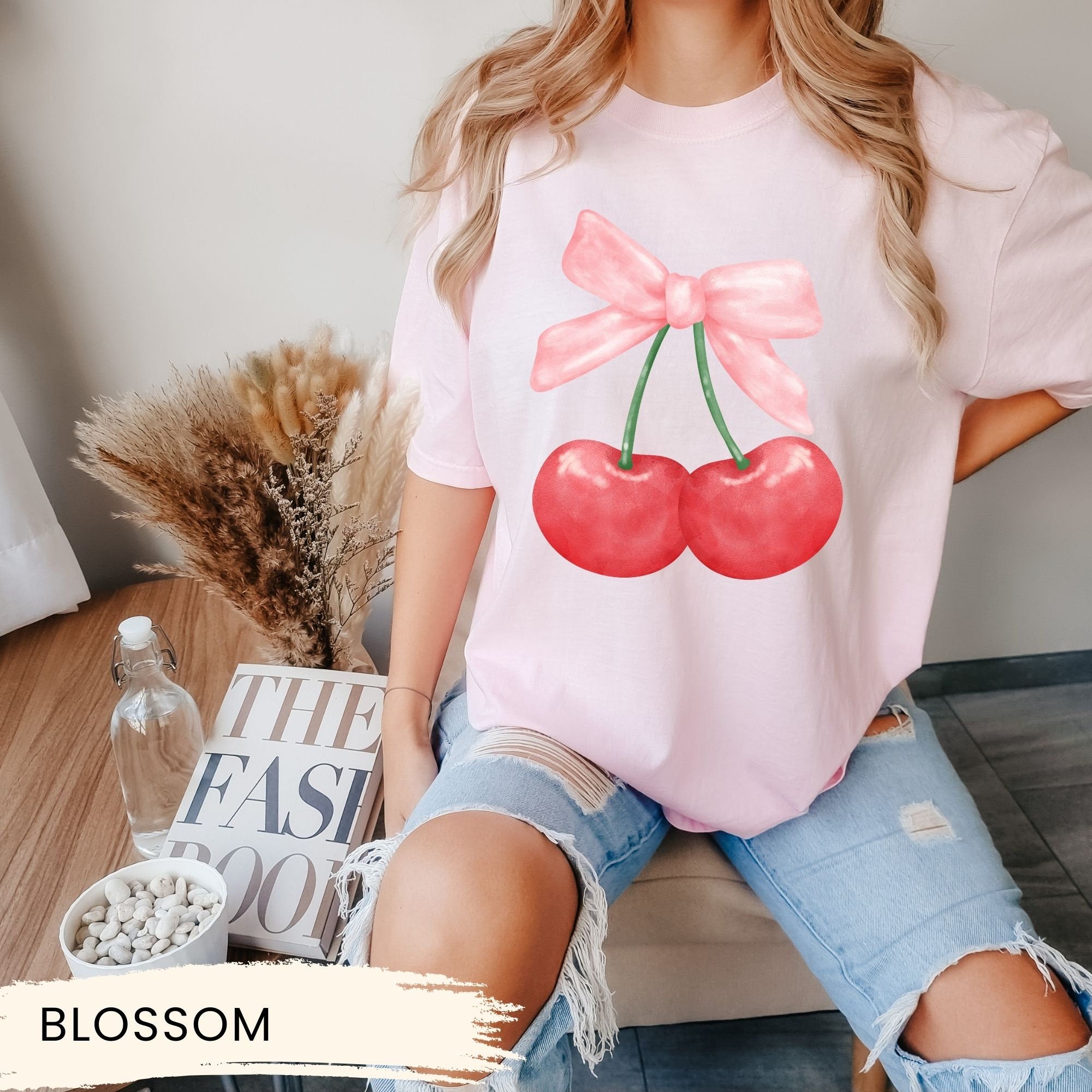 a woman sitting on a table wearing a pink shirt with cherries on it