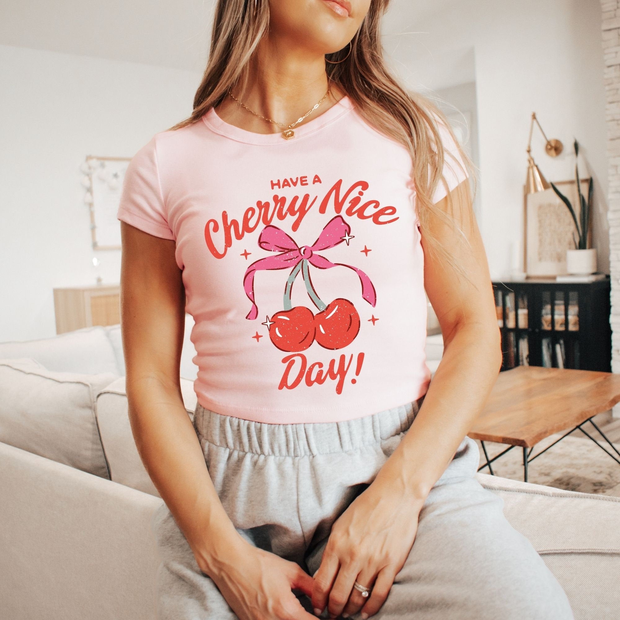 a woman sitting on a couch wearing a pink cherry nice day t - shirt