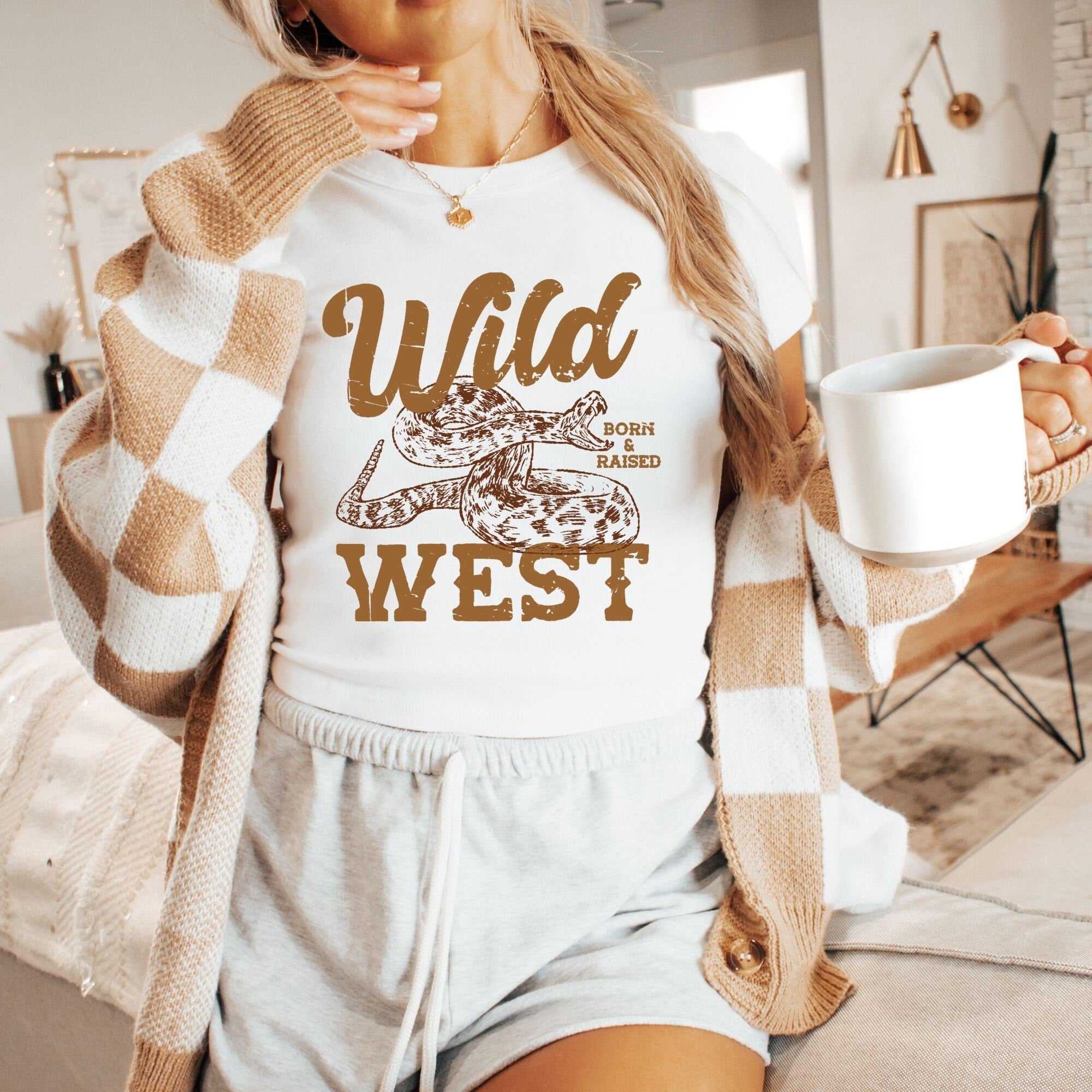 a woman holding a coffee cup and wearing a wild west shirt