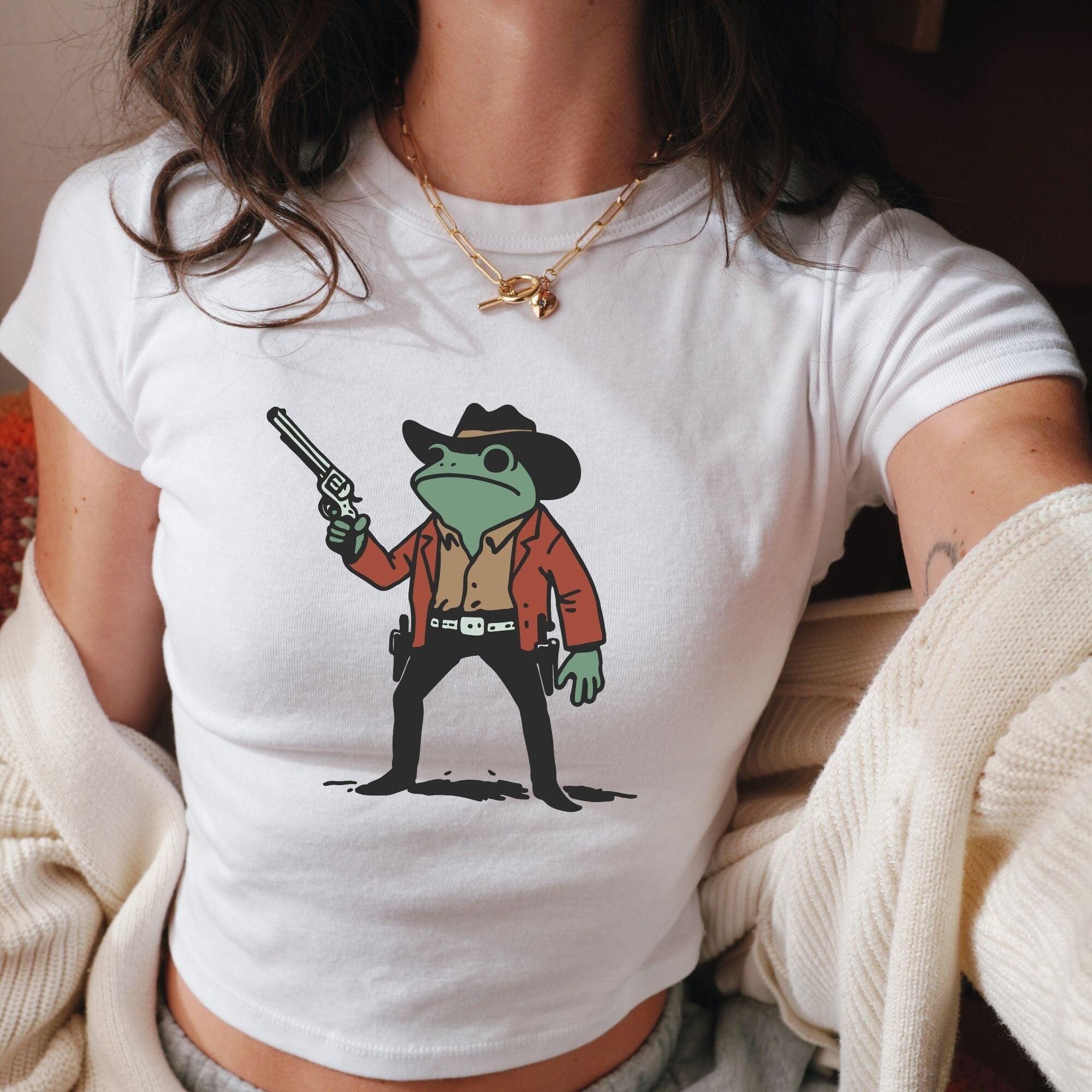 a woman wearing a white shirt with a picture of a frog holding a gun