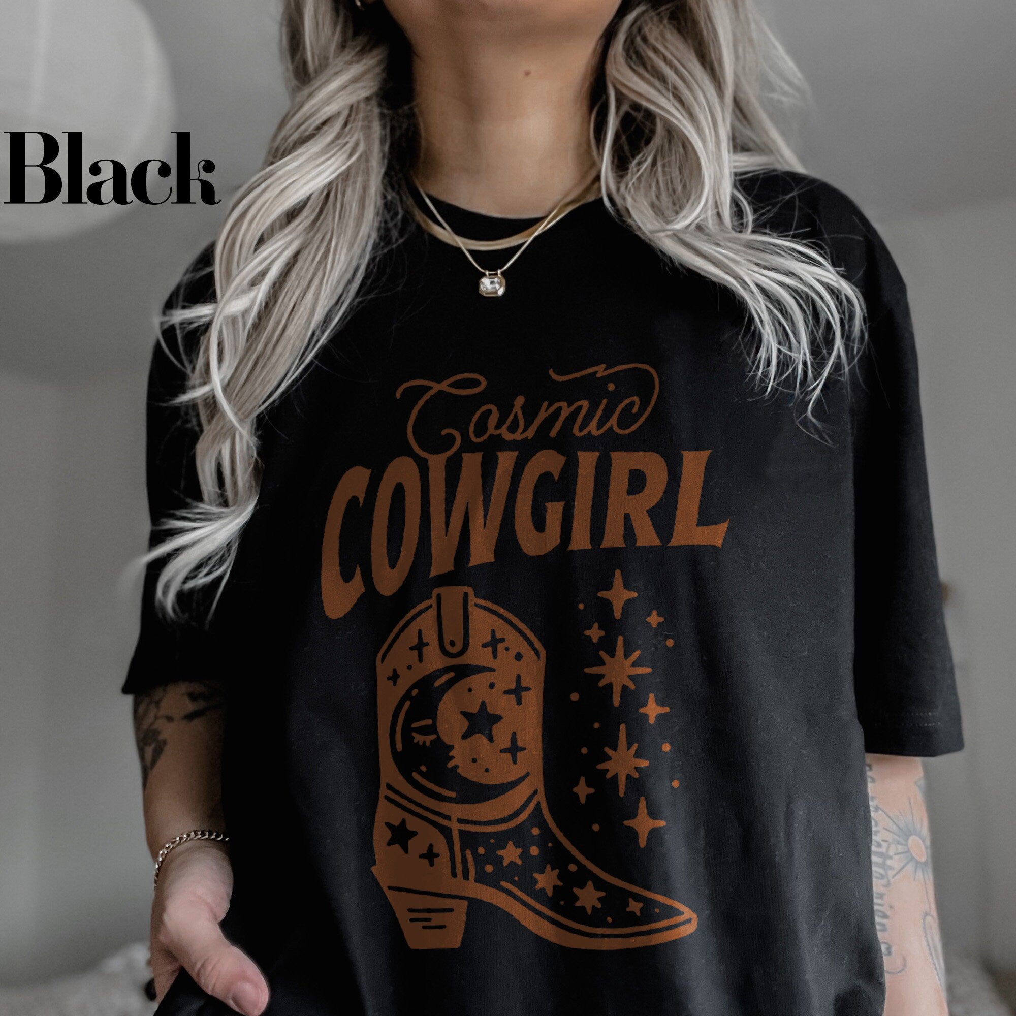 a woman wearing a black t - shirt with the words cosmic cowgirl on it