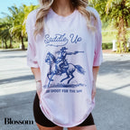 a woman wearing a t - shirt that says saddle up and shoot for the sky