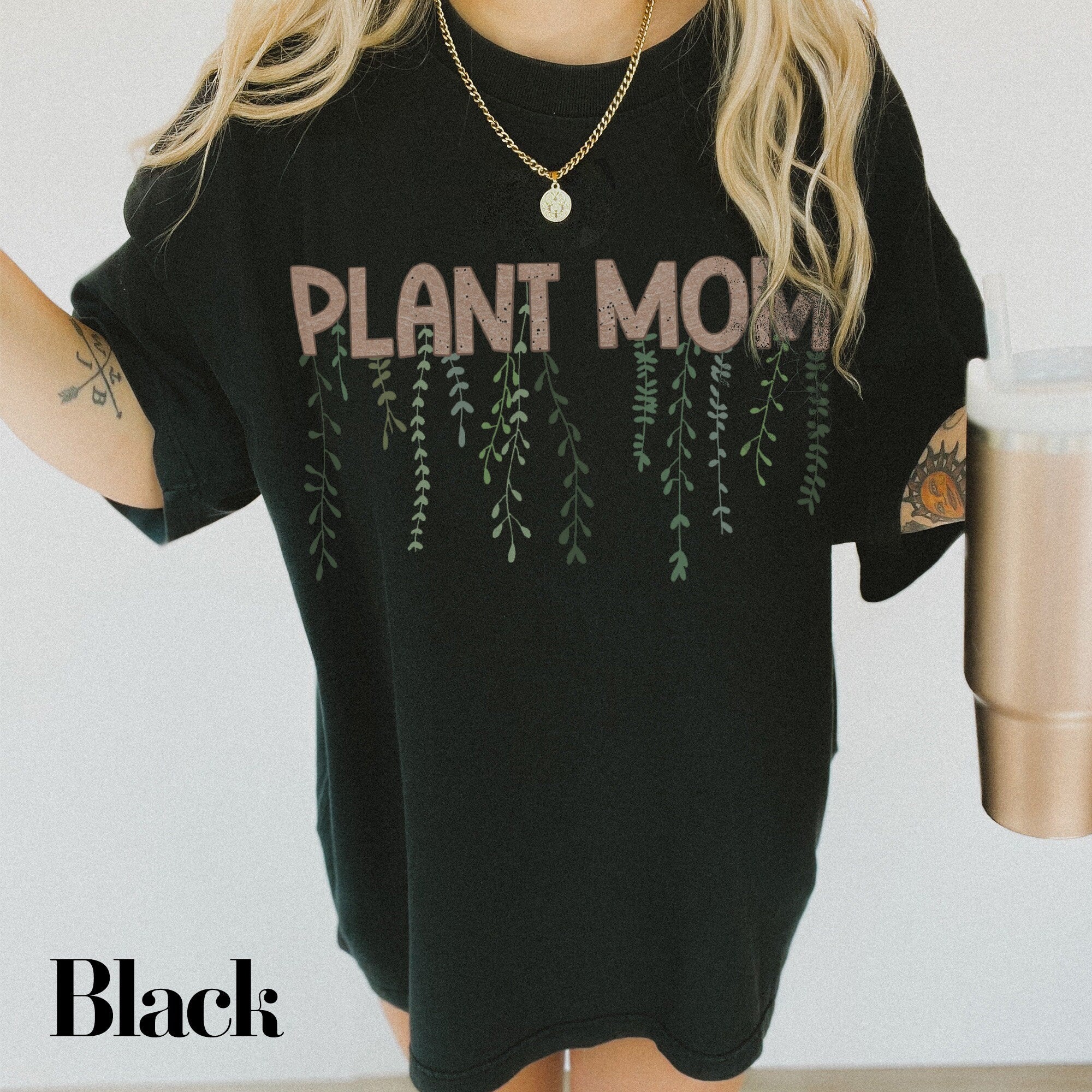 a woman holding a drink and wearing a plant mom shirt